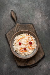 Sauerkraut with cranberries and carrots in a bowl on a wooden cutting board, dark rustic background. Top view, flat lay, vertical. .