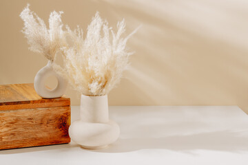 Elegant vase set with copy space. Ceramic vase with pampas grass, wooden storage box on the table with sunlight shadows. Still life composition, scandinavian home interior decoration.