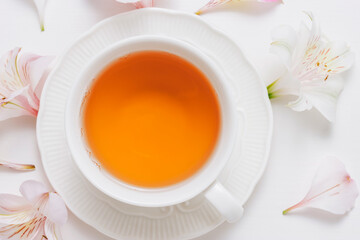 Cup of healthy organic tea close up with flowers at the background, top view.