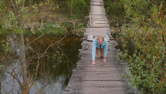 A woman crawls across a rickety suspension bridge. She's afraid to go
