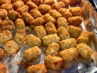 Tater tots cooking on an aluminum foil covered tray in the oven