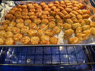 Frozen potato products cooking on an aluminum foil covered tray in the oven