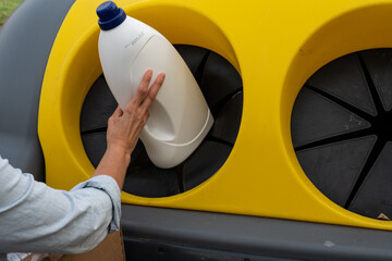 Woman's hand throwing a container into a recycling garbage can. The garbage can has a yellow lid...