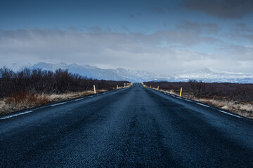 Empty road across Icelandic highlands with snowy mountains on the horizon