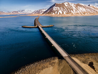 Aerial view of a road across Icelandic fjord with high mountains partially covered with snow 2