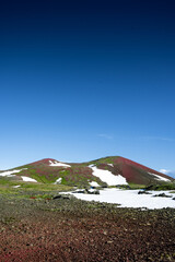 Volcanic hills with red rocks and green grass partially covered with snow 2