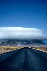Empty asphalt road across Icelandic highlands with a mountain dramatically covered by the cloud