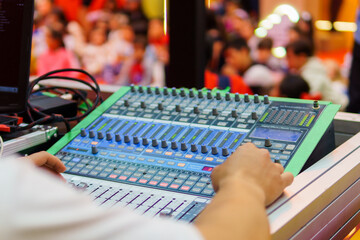 A young DJ mixing sounds and music at an event with many people in an out of focus background