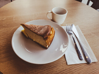 A slice of San Sebastian Cheesecake on a plate with a coffee in a cafe 