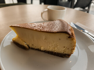 Obraz premium A slice of San Sebastian Cheesecake on a plate with a coffee in a cafe 