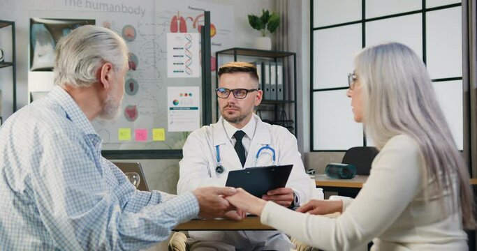 Senior man and woman couple visiting their family doctor in modern clinic. Medicine and healthcare concept.
