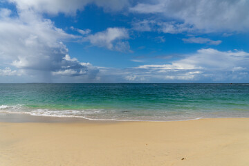 La vue s'étend sur la mer bleue, où le ciel et les nuages se rencontrent à l'horizon, tandis que le sable et les eaux turquoises de la Bretagne sont ornés d'une écume blanche.