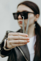 The girl shows tweezers for eyelash extensions.