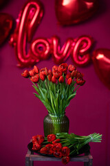 Balloons in the shape of the word love and a bouquet of tulips on a background of red hearts.