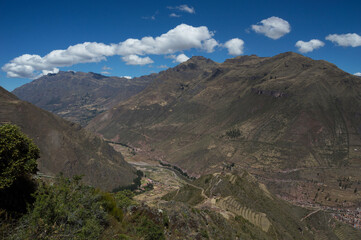 Ruins of the ancient city of Pisac in the distance surrounded by big mountains under blue sky with clouds - obrazy, fototapety, plakaty