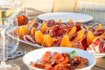 An Italian alfresco dining setting, featuring a plate of Prosciutto paired with sweet melon slices,...