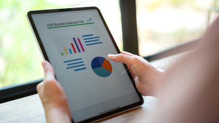 Action of a person hand is touching on tablet screen to review the 2024 business investment plan with graph and chart data. Business working with technology concept, close-up and selective focus.	
