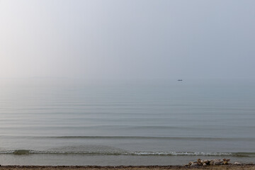A solitary vessel is silhouetted against the serene expanse of Lake Garda, with gentle waves...
