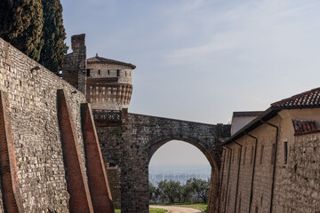 Fototapeta na wymiar View from Brescia historic castle grounds, where the aged stone bridge arch leads to the Torre dei Prigionieri, overlooking the distant cityscape
