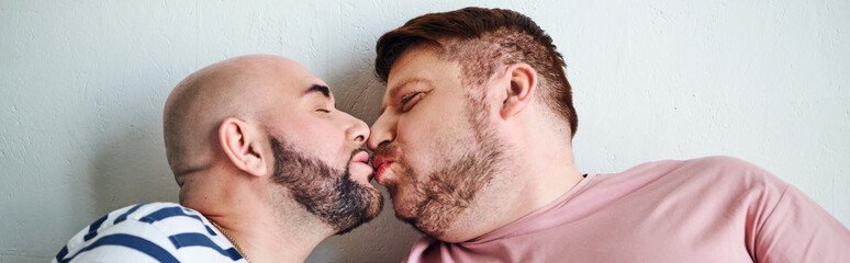 A gay couple expresses affection in front of a wall.