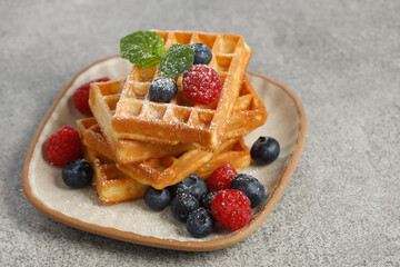 Waffles with berries in plate on grey table	
