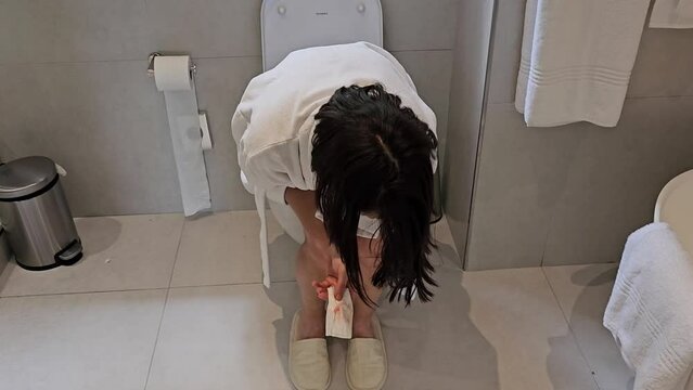 Young woman with hemorrhoids sitting on toilet bowl at home concept