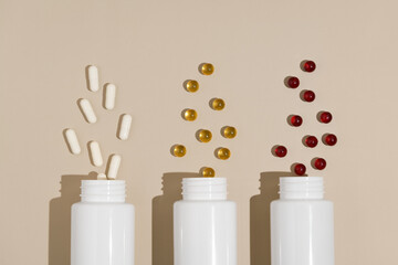 Three white mockup jars with white, yellow and red pill capsules on beige isolated background. Concept of pharmacy, health, dietary supplements and medical products. Image for your design