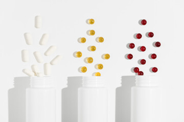 Close-up of three white mockup jars with white, yellow and red capsule pills on white isolated background. Concept of pharmacy, dietary supplements, health care. Image for your design