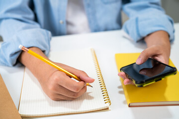 Teenage write in notebook and use mobile phone search data online to online learning university...