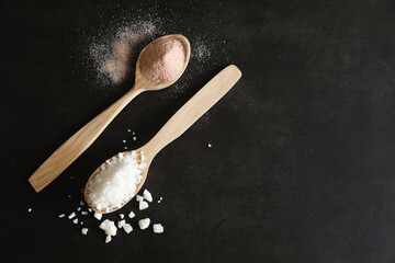 Different types of organic salt in spoons on black table, flat lay. Space for text