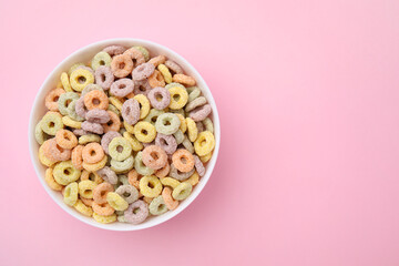 Tasty cereal rings in bowl on pink table, top view. Space for text