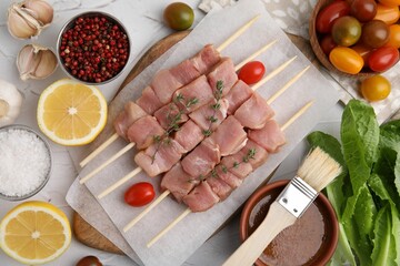 Flat lay composition of skewers with cut raw meat, thyme, tomatoes and marinade on light table