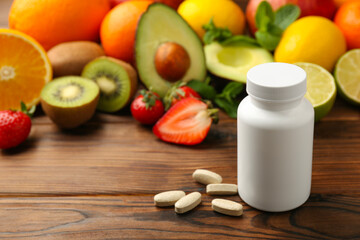 Vitamin pills, bottle and fresh fruits on wooden table. Space for text