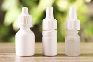 Bottles of medical drops on wooden table against blurred background
