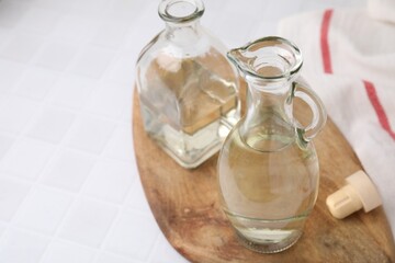 Vinegar in glass jug and bottle on white tiled table, space for text