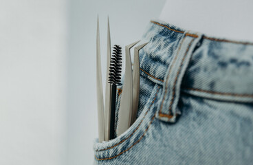 Two tweezers and a brush for eyelash extensions in a jeans pocket.