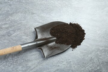 Metal shovel with fertile soil on gray textured surface, above view