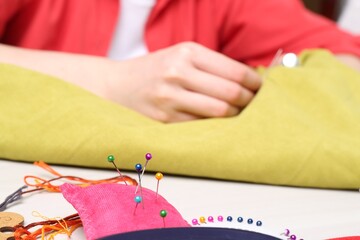 Woman with sewing thread embroidering on cloth at table, focus on pin cushion