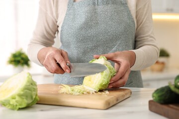 Housewife cutting cabbage at white marble table in kitchen, closeup