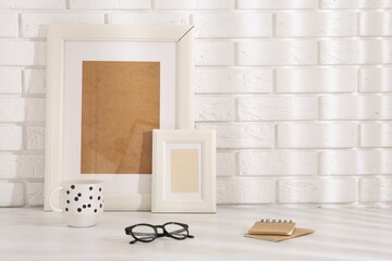 Stylish office workplace. Frames, glasses, cup and notebooks on white table near brick wall