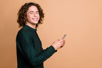 Photo portrait of handsome young guy hold device smile profile dressed stylish green garment isolated on beige color background