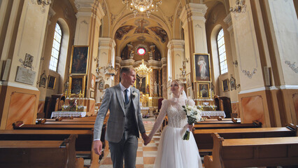 The bride and groom walk through a Catholic church.