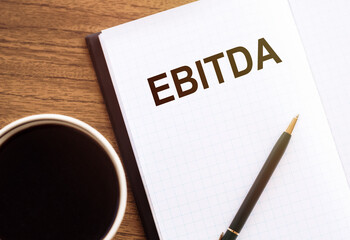 A notepad with the word EBITDA written on it placed next to a cup of coffee.