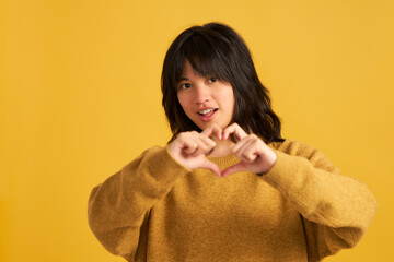 A woman in a yellow sweater is making a heart shape with her hands