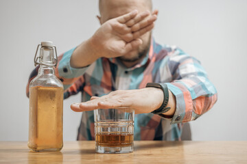Man refusing alcohol, glass with alcohol drink and bottle of whiskey or brandy on a table,...
