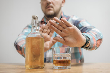 Man refusing alcohol, glass with alcohol drink and bottle of whiskey or brandy on a table, alcoholism and bad habits concept