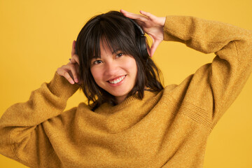 A woman wearing a yellow sweater and headphones is smiling