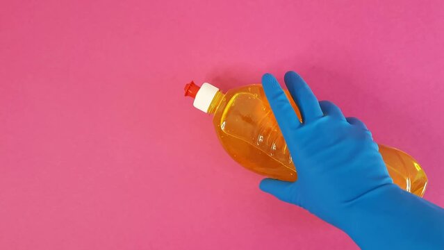 Hand in blue rubber glove takes detergent from pink table. person picks up bottle of household chemicals. Cleaning Services Concept - house, apartment, office cleaning. Template with copy space