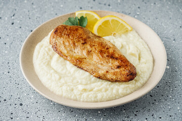 delicious mashed cauliflower and fried chicken breast on a light stone background