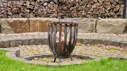 A large fire pit with wood in it sits in front of a stone wall